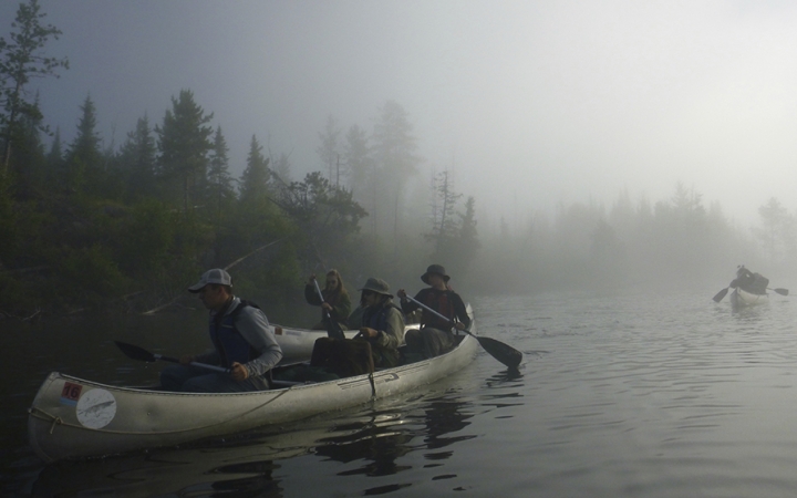 three canoes navigate waters in the morning fog